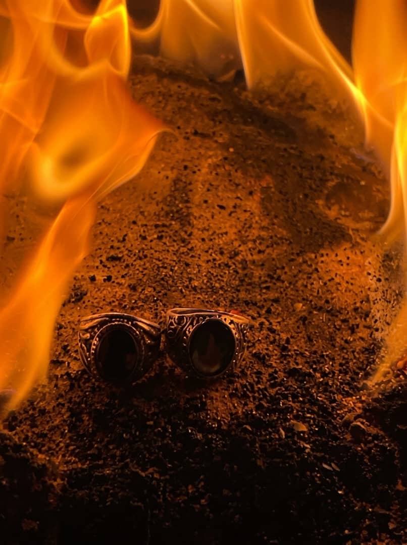 Two silver rings with dark stones resting in glowing embers